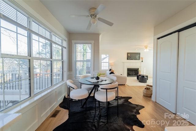 dining area with a fireplace, visible vents, wood finished floors, and wainscoting