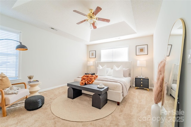 bedroom featuring light carpet, a ceiling fan, visible vents, baseboards, and a tray ceiling