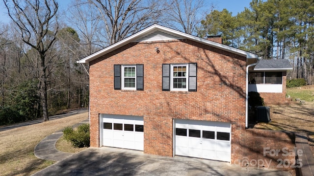 view of side of home featuring driveway, central AC unit, a chimney, an attached garage, and brick siding