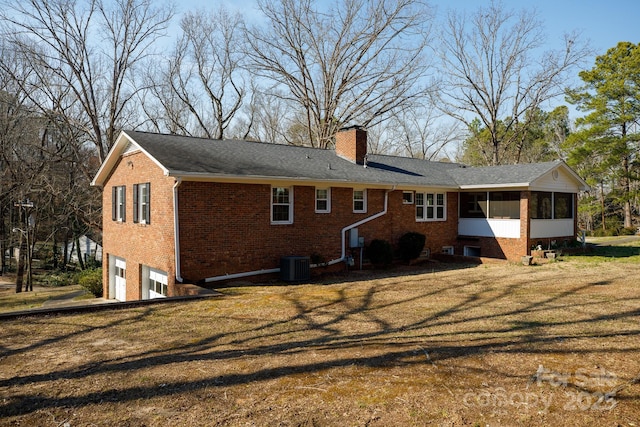 rear view of house with a sunroom, a chimney, an attached garage, cooling unit, and brick siding