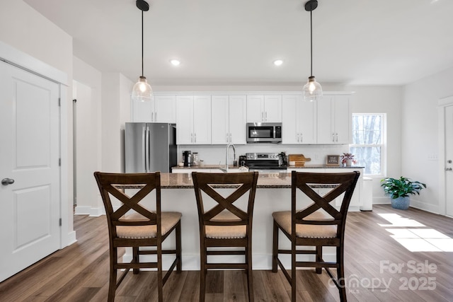 kitchen with stainless steel appliances, white cabinetry, a kitchen bar, and wood finished floors