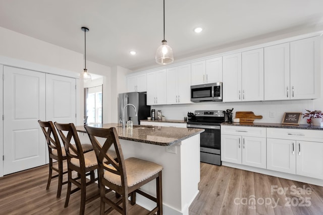 kitchen with stainless steel appliances, a center island with sink, light wood-style flooring, and a sink