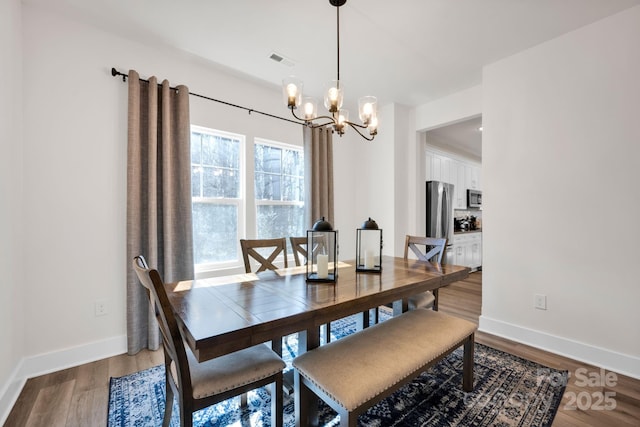 dining space with baseboards, visible vents, a chandelier, and wood finished floors