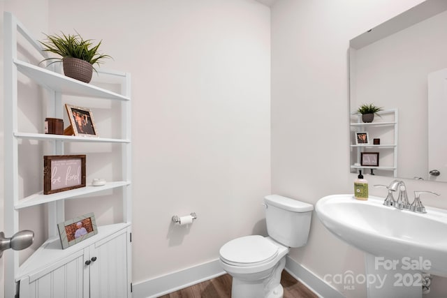 half bath with wood finished floors, a sink, toilet, and baseboards