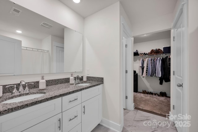 full bathroom with a walk in closet, marble finish floor, a sink, and double vanity