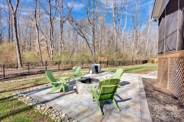 view of patio featuring a wooded view, an outdoor fire pit, and a fenced backyard