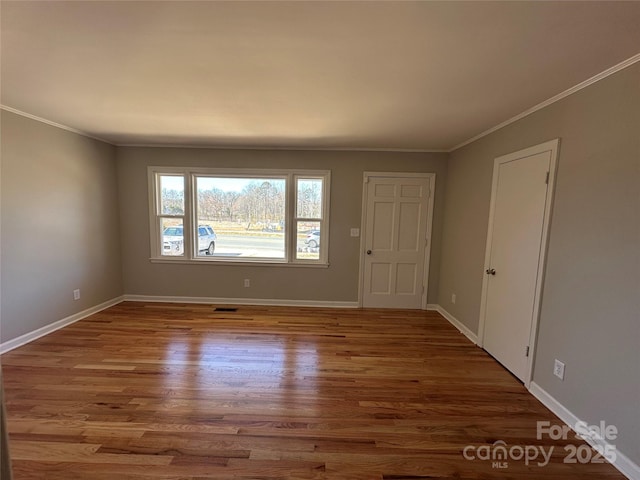 unfurnished room featuring baseboards, wood finished floors, visible vents, and crown molding