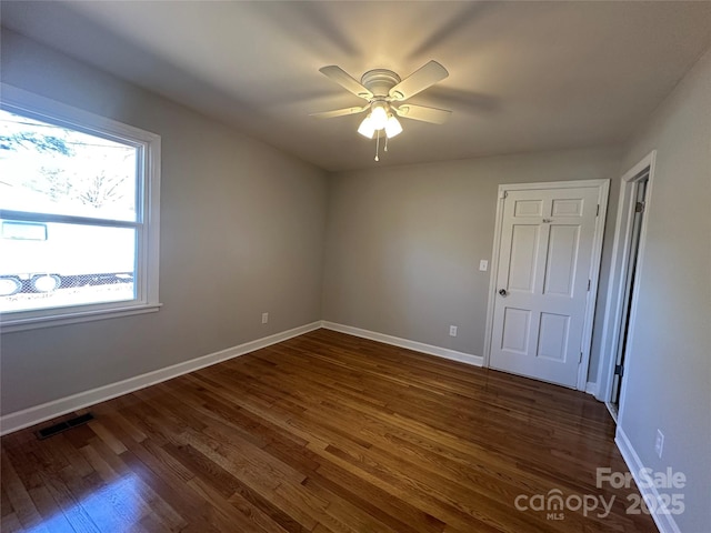 spare room with dark wood-style floors, a ceiling fan, visible vents, and baseboards