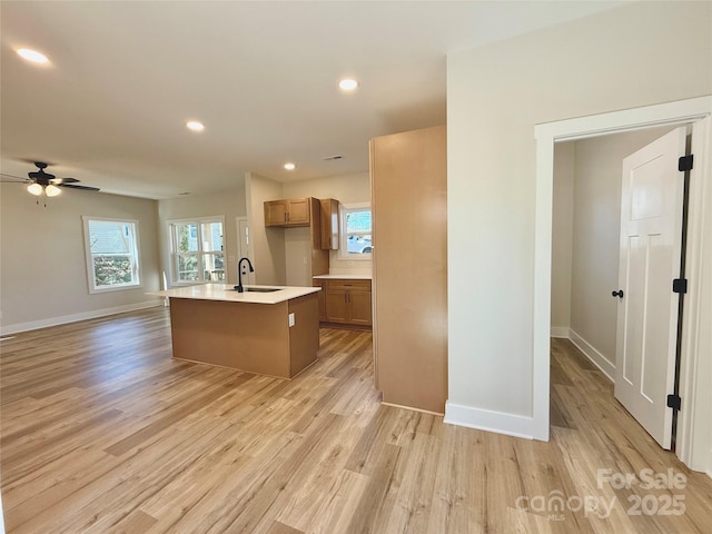 kitchen with light countertops, light wood finished floors, a sink, and a center island with sink