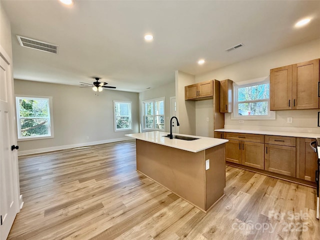 kitchen with an island with sink, visible vents, light countertops, and a sink