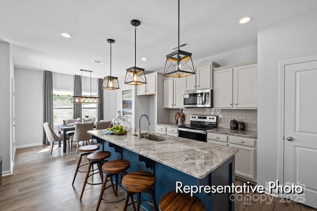 kitchen with visible vents, appliances with stainless steel finishes, hanging light fixtures, a kitchen island with sink, and a sink