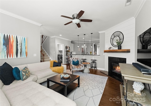 living area featuring visible vents, wood finished floors, a fireplace, crown molding, and stairs