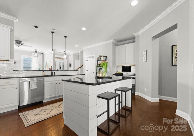 kitchen with dark countertops, a kitchen breakfast bar, a peninsula, stainless steel dishwasher, and a sink