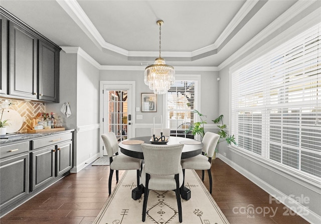 dining room featuring a notable chandelier, dark wood-type flooring, baseboards, crown molding, and a raised ceiling