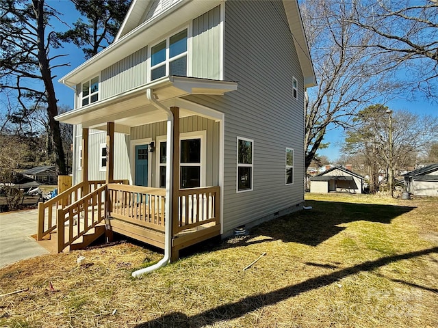 view of side of property with board and batten siding, crawl space, a porch, and a lawn