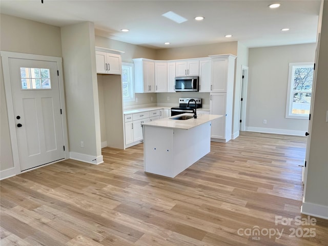 kitchen with stainless steel appliances, light countertops, light wood-style floors, white cabinetry, and an island with sink