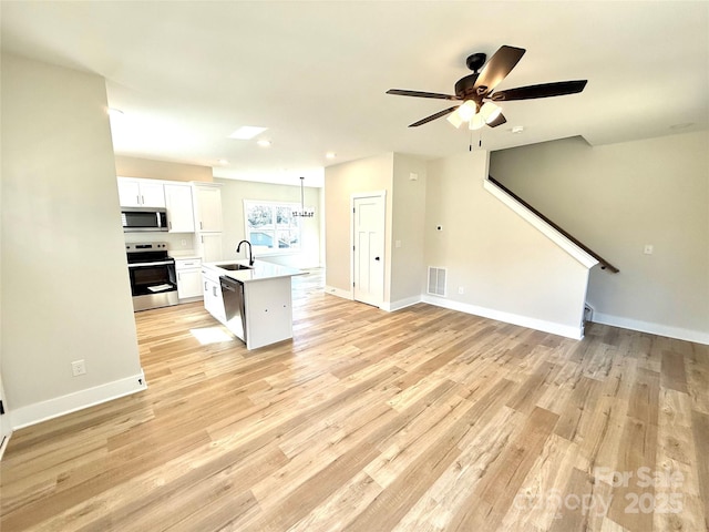 kitchen with a center island with sink, light countertops, hanging light fixtures, appliances with stainless steel finishes, and white cabinetry