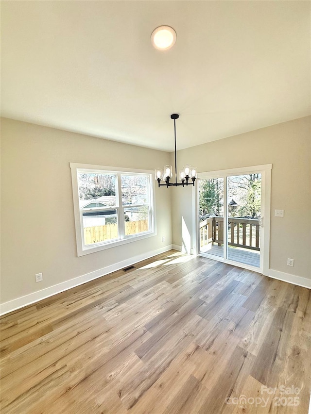 unfurnished dining area with a healthy amount of sunlight, visible vents, light wood finished floors, and an inviting chandelier