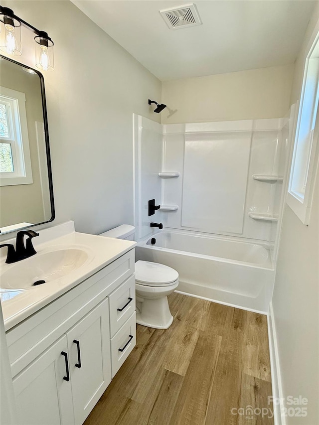 full bath with visible vents, toilet, wood finished floors, vanity, and washtub / shower combination