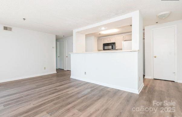 unfurnished living room with wood finished floors, visible vents, and baseboards