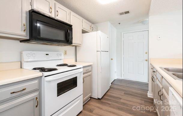 kitchen with a textured ceiling, white appliances, visible vents, white cabinets, and light countertops