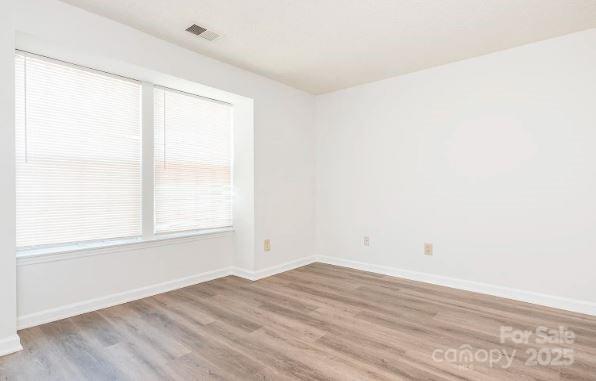 empty room with light wood finished floors, visible vents, and baseboards