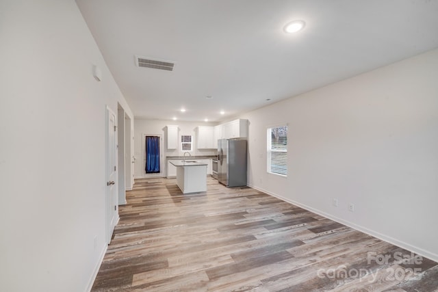 interior space with visible vents, open floor plan, white cabinetry, a kitchen island, and stainless steel fridge