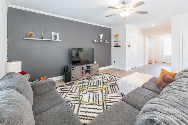 living room featuring light wood-style flooring, baseboards, ceiling fan, and crown molding