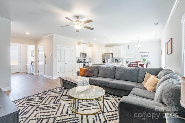 living area featuring recessed lighting, wood finished floors, visible vents, baseboards, and ornamental molding