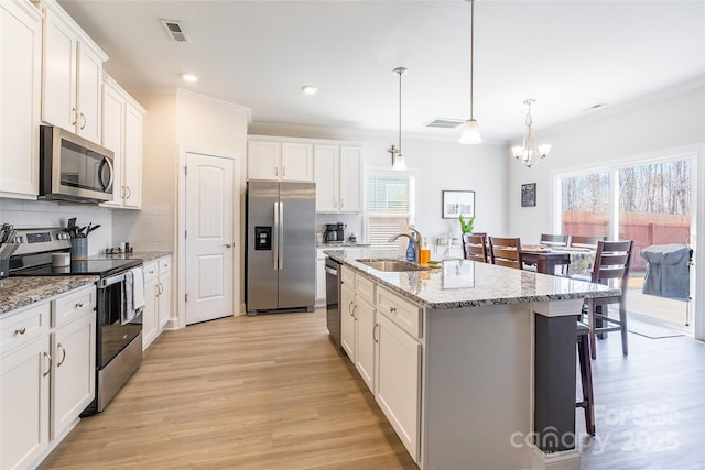 kitchen with a center island with sink, visible vents, appliances with stainless steel finishes, hanging light fixtures, and white cabinetry