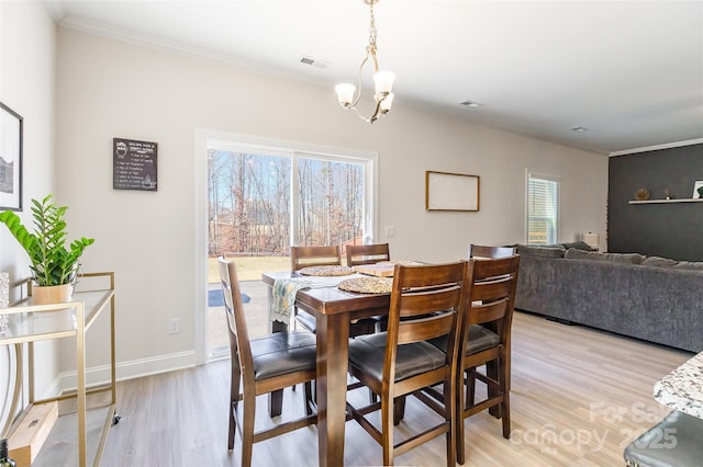 dining area with baseboards, ornamental molding, light wood-type flooring, and an inviting chandelier
