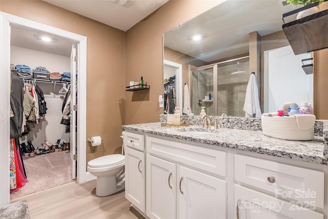 full bathroom featuring a walk in closet, toilet, a stall shower, vanity, and wood finished floors