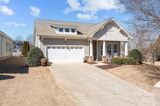 view of front facade featuring driveway, stone siding, an attached garage, and covered porch