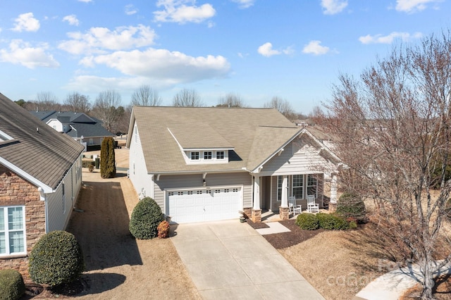 view of front of home featuring a garage, stone siding, covered porch, and driveway