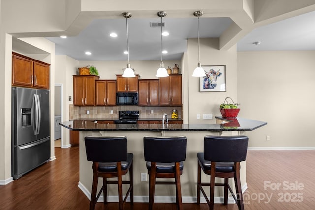 kitchen featuring hanging light fixtures, decorative backsplash, dark wood-style floors, black appliances, and a kitchen bar