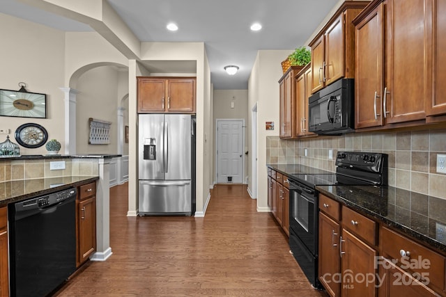 kitchen with dark stone counters, decorative backsplash, brown cabinets, dark wood-style floors, and black appliances