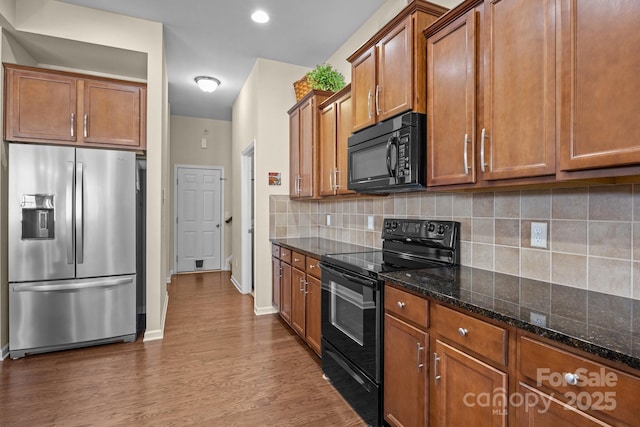 kitchen featuring brown cabinets, decorative backsplash, dark wood-style floors, black appliances, and dark stone countertops