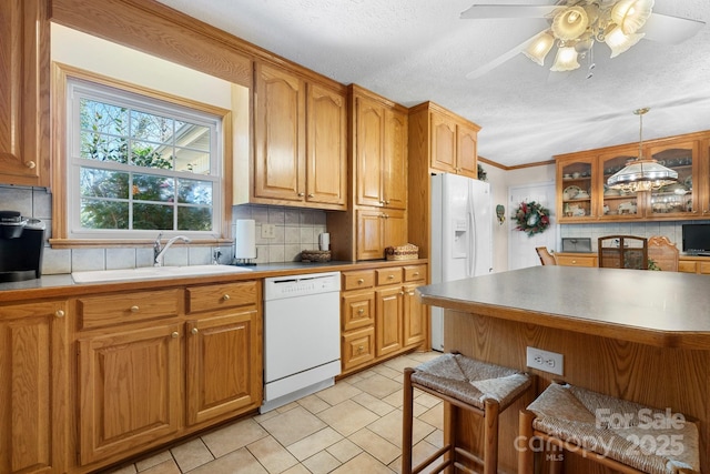 kitchen featuring a breakfast bar, backsplash, glass insert cabinets, a sink, and white appliances