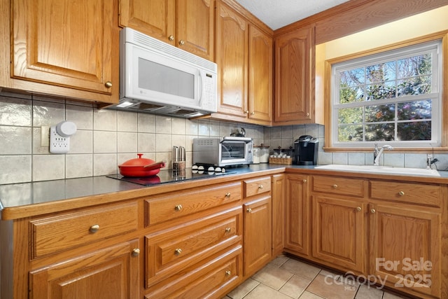 kitchen with light tile patterned floors, a toaster, white microwave, a sink, and backsplash