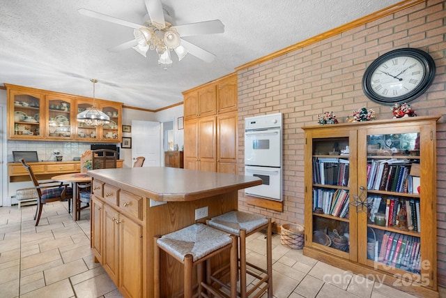 kitchen with double oven, a kitchen island, glass insert cabinets, and a textured ceiling