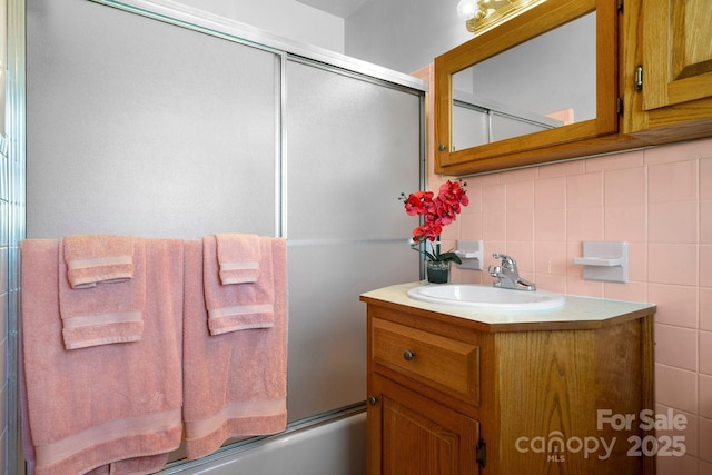 bathroom featuring tile walls, vanity, and bath / shower combo with glass door