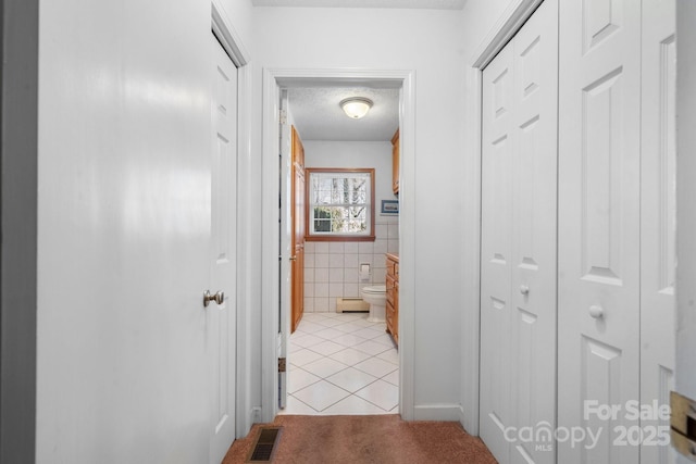 corridor featuring a textured ceiling, light tile patterned flooring, light carpet, visible vents, and tile walls