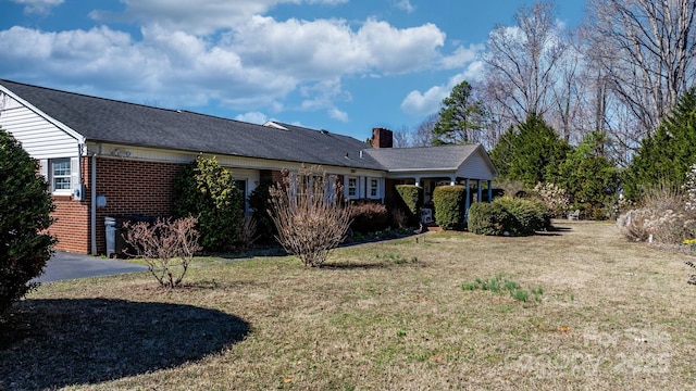 exterior space with a chimney, a lawn, and brick siding