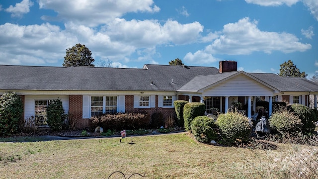 view of front of property featuring roof with shingles, a chimney, a front lawn, and brick siding