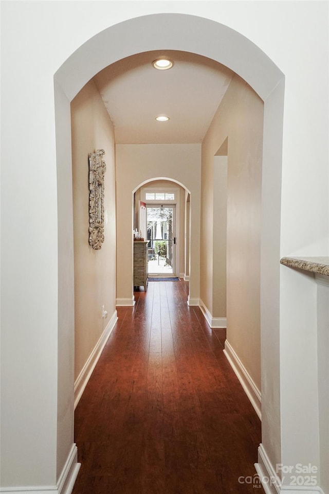 corridor featuring arched walkways, recessed lighting, wood finished floors, and baseboards