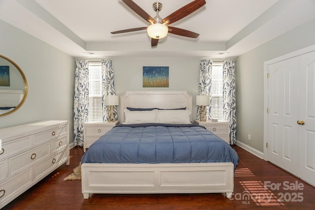 bedroom featuring a ceiling fan, baseboards, a tray ceiling, and wood finished floors