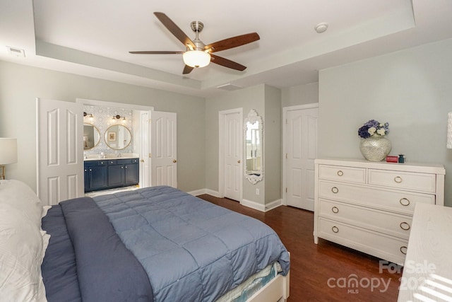 bedroom featuring ensuite bathroom, dark wood-style flooring, visible vents, baseboards, and a tray ceiling