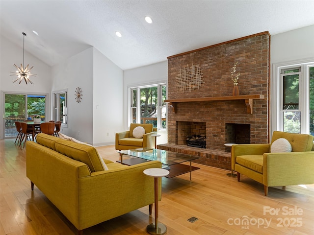 living room with a brick fireplace, a notable chandelier, light wood-style flooring, and a textured ceiling