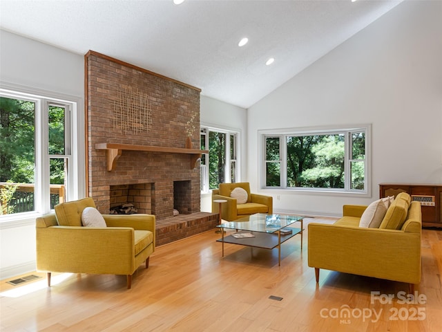 living area with high vaulted ceiling, light wood finished floors, a fireplace, and visible vents