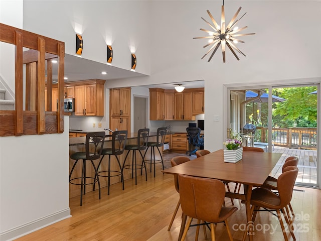 dining space featuring a towering ceiling, light wood-style flooring, and a notable chandelier